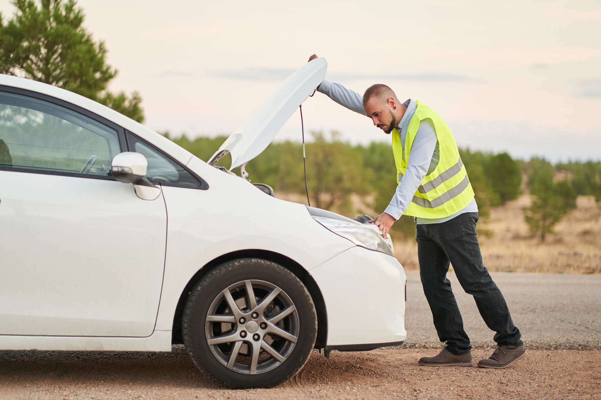 a man looking at the engine of his car wearing an emergency vest because it has broken down Cosa fare se il volante vibra